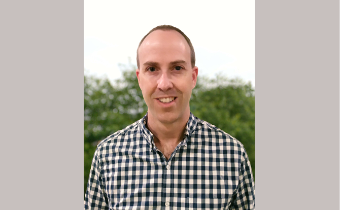 Headshot of a man with checkered shirt in front of a natural landscape