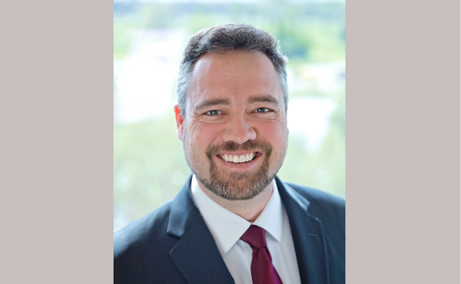 Headshot of man with white collared shirt, red tie, and blue suit jacket