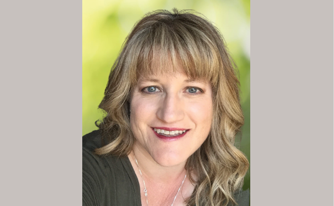 Headshot of women with blonde hair and bangs in from of a natural landscape