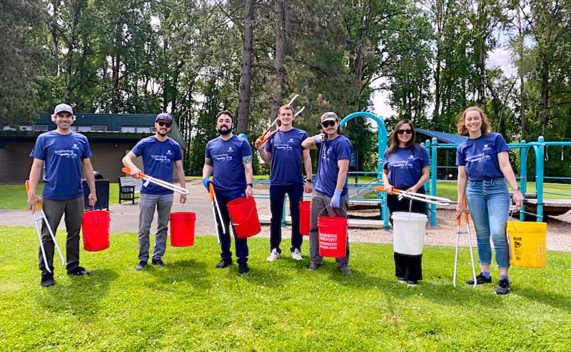 Group of 7 people carrying buckets and grabbers to pick up trash in a park