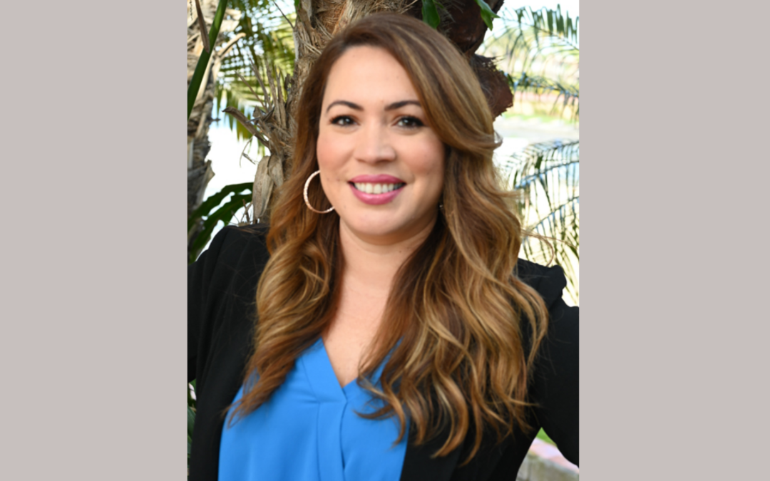 Headshot of a woman in a blue shirt in front of palm trees